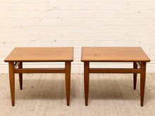 Load image into Gallery viewer, A pair of mid-century modern wooden end tables with square tops and tapered legs, set against a white brick wall and textured beige rug.
