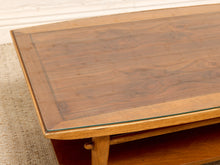 Load image into Gallery viewer, A close-up of a mid-century modern wooden coffee table with a glass top, showcasing a rich walnut-like wood grain finish and a glass inset border.
