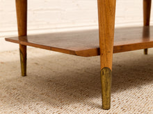 Load image into Gallery viewer, Close-up of a mid-century modern wooden coffee table with brass metal leg caps, set on a textured beige rug against a white brick wall.
