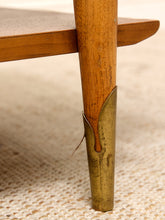 Load image into Gallery viewer, Close-up of a wooden table leg with a brass metal foot protector on a beige woven rug.
