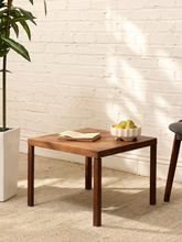 Load image into Gallery viewer, A square wooden side table with dark brown legs and a medium brown wood top, styled in a bright room with a white brick wall, a potted plant, and a bowl of fruit on top.
