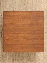 Load image into Gallery viewer, A square wooden board or tabletop with a warm medium-brown wood grain finish, photographed from directly above on a textured beige woven rug.
