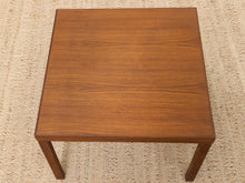 Load image into Gallery viewer, A square wooden side table with a warm medium-brown finish and visible wood grain, shown from a top-down angle on a woven beige rug.
