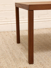 Load image into Gallery viewer, Close-up of a dark brown wooden table leg standing on a woven beige rug against a white brick wall.
