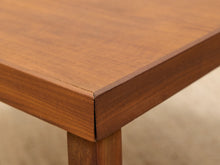 Load image into Gallery viewer, Close-up detail of a wooden table corner showing the grain and finish of the wood, with a beige carpeted floor in the background.
