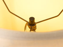 Load image into Gallery viewer, Close-up of a brass lamp shade finial and metal shade support arms against a warm yellow glowing background.

