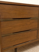 Load image into Gallery viewer, Close-up of a mid-century modern wooden dresser with three drawers, featuring a warm medium-brown wood finish and slim dark metal pull handles.
