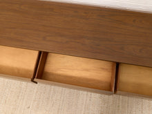 Load image into Gallery viewer, Close-up of a mid-century modern wooden media console with a dark walnut top and open drawers showing light wood interiors, set on a textured beige rug.
