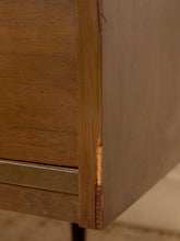 Load image into Gallery viewer, Close-up detail of a mid-century modern wooden cabinet corner, showcasing the warm brown wood grain, a brass pull handle, and a brass corner brace.
