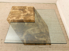 Load image into Gallery viewer, A modern geometric coffee table featuring a clear glass top layered over a sculptural, stepped base made of marbled stone in earthy brown and beige tones, set on a textured beige rug.
