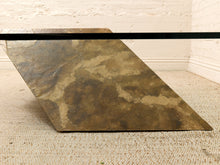 Load image into Gallery viewer, A square stone slab table base with a rustic, mottled finish in earthy brown, bronze, and beige tones, shown resting on a beige carpet against a white brick wall.
