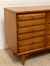 Load image into Gallery viewer, Mid-century modern wooden chest of drawers with six drawers, brass knobs, and tapered legs, set against a white brick wall and woven rug.
