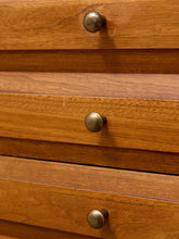 Load image into Gallery viewer, Close-up of a wooden dresser with three drawers and round metallic knobs, showing warm brown wood grain and brass-toned hardware.
