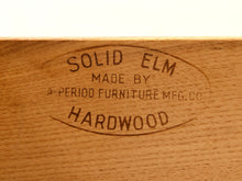 Load image into Gallery viewer, Close-up of a wooden surface with engraved text reading 'SOLID ELM MADE BY PERIOD FURNITURE MFG.CO HARDWOOD'.

