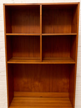 Load image into Gallery viewer, A mid-century modern wooden bookcase with a warm reddish-brown finish, featuring a two-tiered upper section with a central divider and a three-tier lower section, set against a white brick wall.
