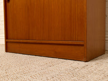 Load image into Gallery viewer, Close-up of a mid-century modern wooden cabinet or bookcase with a warm medium-brown finish, featuring a horizontal drawer front and a textured beige carpet underneath.
