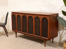 Load image into Gallery viewer, Mid-century modern wooden sideboard cabinet with five arched wire-front doors, shown in a styled room setting against a white brick wall.
