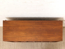 Load image into Gallery viewer, A top-down view of a rectangular wooden chest or cabinet with a rich walnut finish, set against a white brick wall and a beige woven rug.

