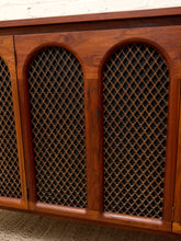 Load image into Gallery viewer, Close-up of a wooden cabinet or sideboard with three arched metal mesh panels on the front, showing warm medium-brown wood grain and dark mesh screens.
