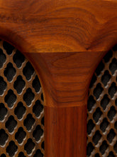 Load image into Gallery viewer, Close-up of a wooden chair or stool showing a rich reddish-brown wood grain on the seat and backrest, meeting a perforated cane or rattan panel.
