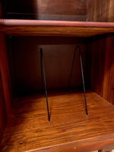 Load image into Gallery viewer, A pair of black metal wire bookends standing on a wooden shelf inside a wooden cabinet or shelf unit.
