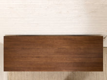 Load image into Gallery viewer, A rectangular dark brown wooden tabletop or desk top with visible wood grain, photographed from above against a white painted brick wall and light rug.
