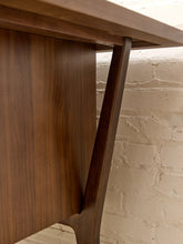 Load image into Gallery viewer, Close-up of a dark brown wooden table leg and apron panel, showing the wood grain and construction against a white brick wall background.
