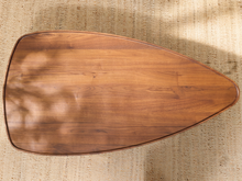 Load image into Gallery viewer, A teardrop-shaped wooden table top with a rich medium-brown wood grain finish, photographed from directly above on a textured beige woven rug.
