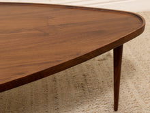 Load image into Gallery viewer, Close-up of a mid-century modern wooden coffee table with a rounded triangular top and tapered legs, showing the rich grain of the dark brown wood on a textured beige rug.

