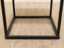 Load image into Gallery viewer, Close-up of a black metal table frame base on a textured beige woven rug.
