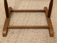Load image into Gallery viewer, Close-up of the wooden base and lower legs of a rocking chair on a textured beige woven rug.
