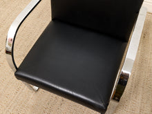 Load image into Gallery viewer, A close-up of a modern black leather chair with a curved polished chrome armrest, shown on a beige woven rug.
