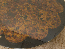 Load image into Gallery viewer, A close-up of a round table featuring a scalloped patterned top in black and warm brown tones, resting on a textured beige woven surface.
