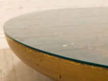 Load image into Gallery viewer, Close-up of a round table featuring a distressed yellow-gold painted base and a clear glass top, with a light neutral background.
