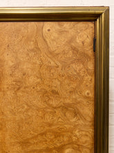 Load image into Gallery viewer, A close-up of a decorative door featuring dramatic, swirling burl wood grain in warm golden-brown tones, framed by a thick metallic gold border.
