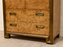 Load image into Gallery viewer, A close-up of a wooden dresser with a rich burl wood grain finish and antique brass drawer pulls, set against a white brick wall and textured carpet.
