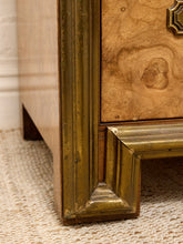 Load image into Gallery viewer, Close-up detail of an antique-style wooden cabinet corner, showing a gold-painted frame, natural burl wood drawer front, and woven beige rug.
