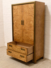 Load image into Gallery viewer, A tall vintage-style cabinet with two upper doors and two lower drawers, covered in warm golden-brown burl wood with brass-toned metal handles and trim, photographed against a white brick wall and light carpet.
