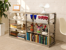 Load image into Gallery viewer, A tall, narrow mirrored sideboard or bookcase with a silver metal frame, styled with books, colorful vases, wine glasses, and small figurines in a bright room with a white brick wall and beige carpet.
