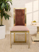 Load image into Gallery viewer, A mid-century modern dining chair with a gold metal frame, a brown velvet backrest, and a textured blush pink upholstered seat cushion, set against a white brick wall.
