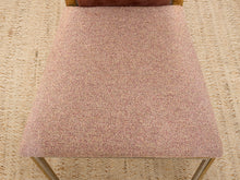 Load image into Gallery viewer, A close-up of a textured upholstered chair seat in a dusty rose pink fabric, with a woven beige rug visible underneath.
