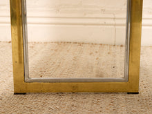 Load image into Gallery viewer, Close-up of a brass-framed mirror with a silver inner trim, resting on a beige woven rug against a white wall.
