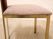 Load image into Gallery viewer, A close-up of a dining chair featuring a textured, heathered pink and beige upholstered seat cushion, a distressed brass frame, and a dark brown wooden backrest, set against a white brick wall and light beige rug.
