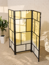 Load image into Gallery viewer, A three-panel folding room divider with a black metal frame and translucent yellow panels, set in a room with a white brick wall, beige carpet, and a potted plant.
