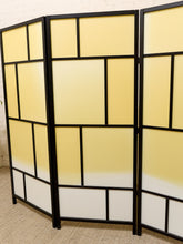 Load image into Gallery viewer, A three-panel folding room divider with a black metal frame and frosted panels that fade from pale yellow at the top to white at the bottom, set against a white brick wall and beige carpet.
