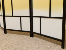Load image into Gallery viewer, A folding Japanese-style screen with black metal frames and frosted panels in yellow and white, standing on a beige textured carpet.
