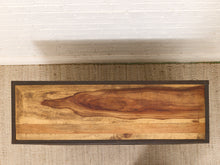 Load image into Gallery viewer, A rectangular wooden board or tray with a natural live-edge wood grain design and a dark border, displayed on a woven rug against a white brick wall.
