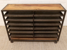 Load image into Gallery viewer, A rustic industrial rolling storage cabinet with a light brown wood top, dark brown metal frame, and multiple horizontal shelves, set on a textured beige rug against a white brick wall.
