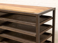 Load image into Gallery viewer, A rustic industrial shelving unit with a light brown wood top and dark brown metal frame and shelves, set against a white brick wall.
