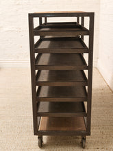 Load image into Gallery viewer, A dark brown rolling storage cart with six tiers, featuring a wood-look top and bottom shelves, set against a white brick wall and beige carpet.
